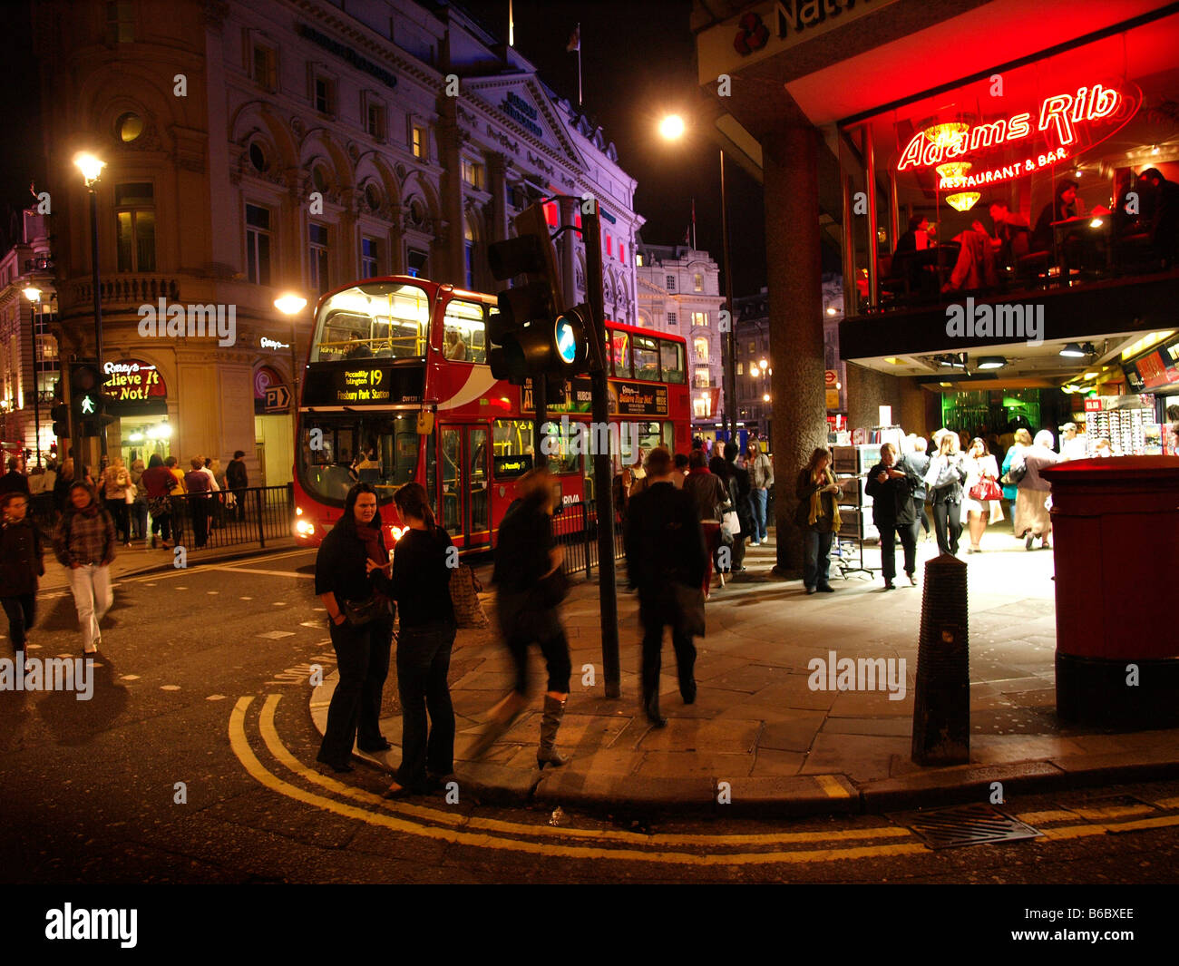 London nightlife colourful lights streetcorner with many people and red bus west end London UK Stock Photo