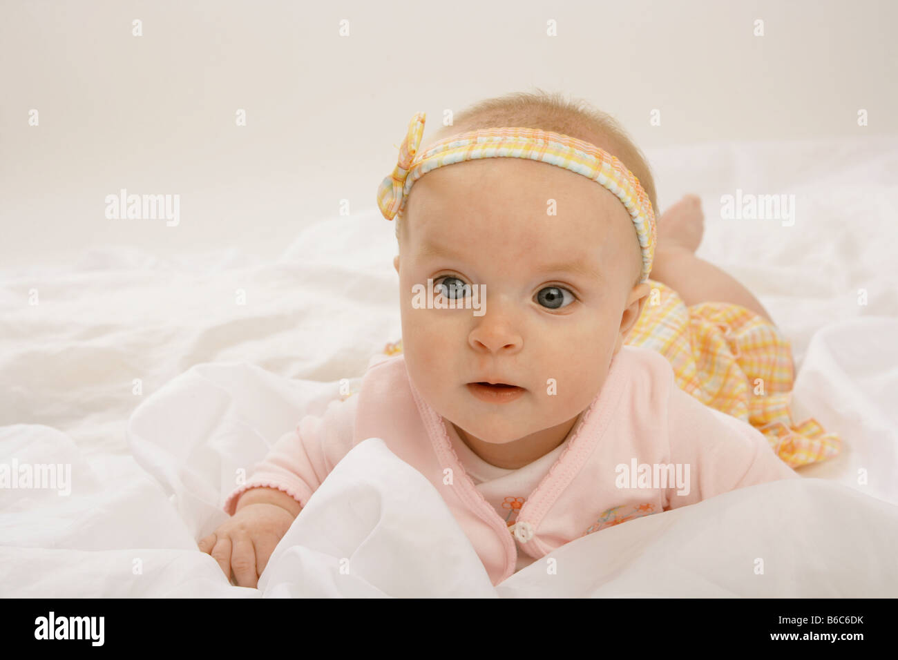 A six month old baby lying on her front on white fabric dressed in pink