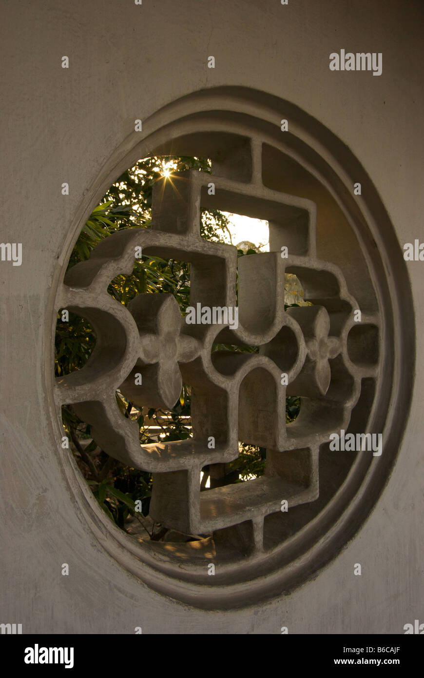 Diffuse light through a stone latticework window softly illuminates a courtyard at the Master of Nets Garden Stock Photo