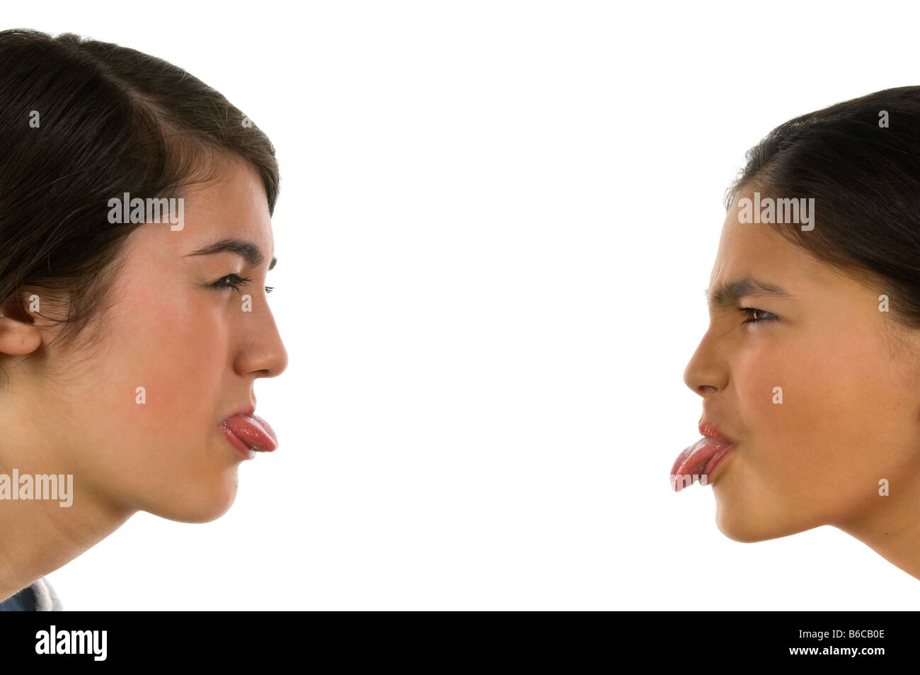 Horizontal close up portrait of two teenage sisters poking their tongues out during a fight against a white background Stock Photo