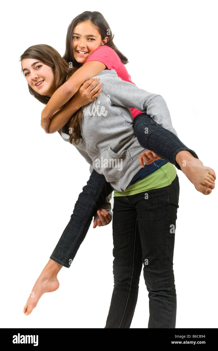 Vertical close up portrait of two teenage girls one giving the other a piggy back ride against a white background. Stock Photo