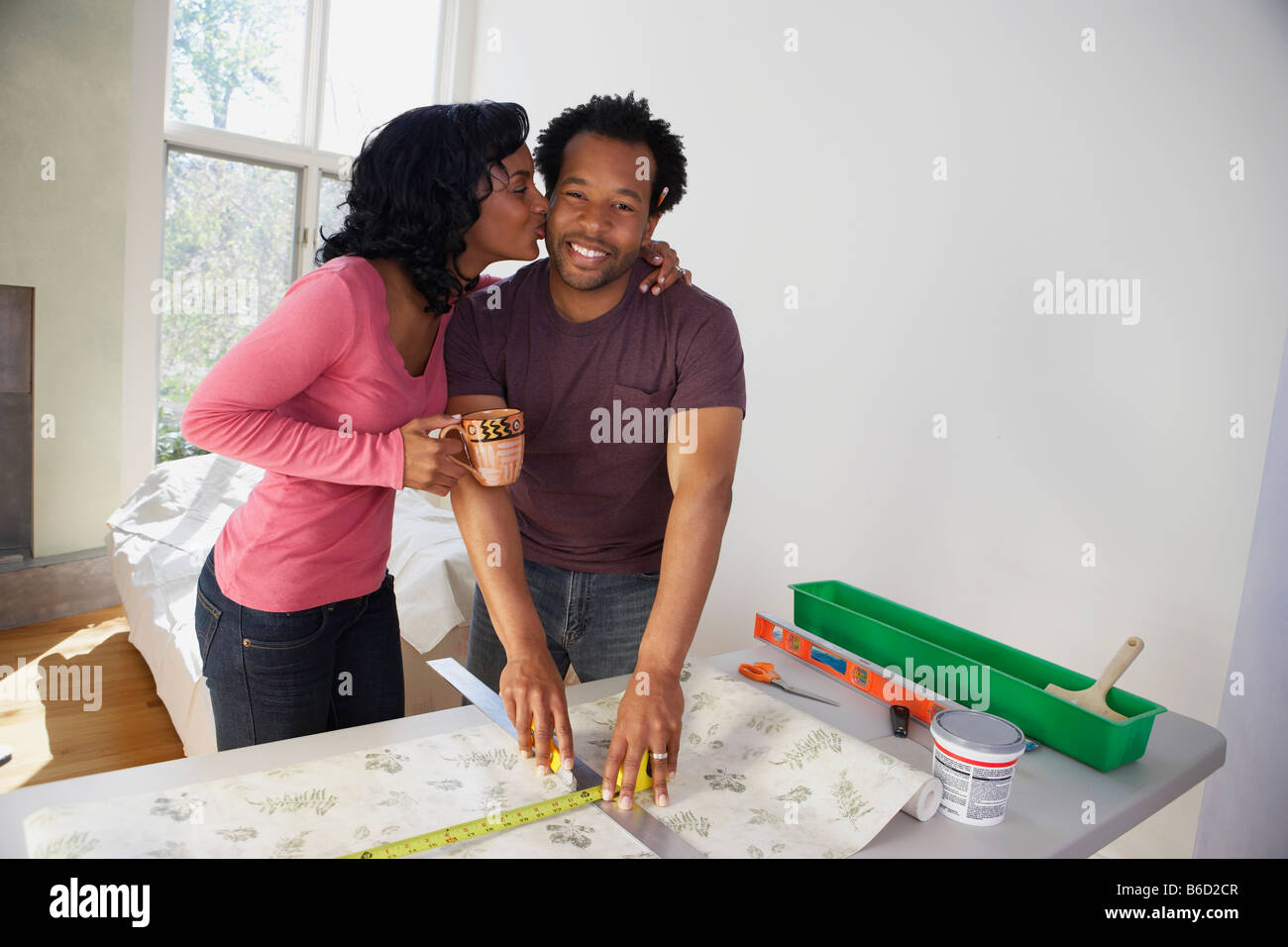 African man measuring wall paper getting kiss from wife Stock Photo