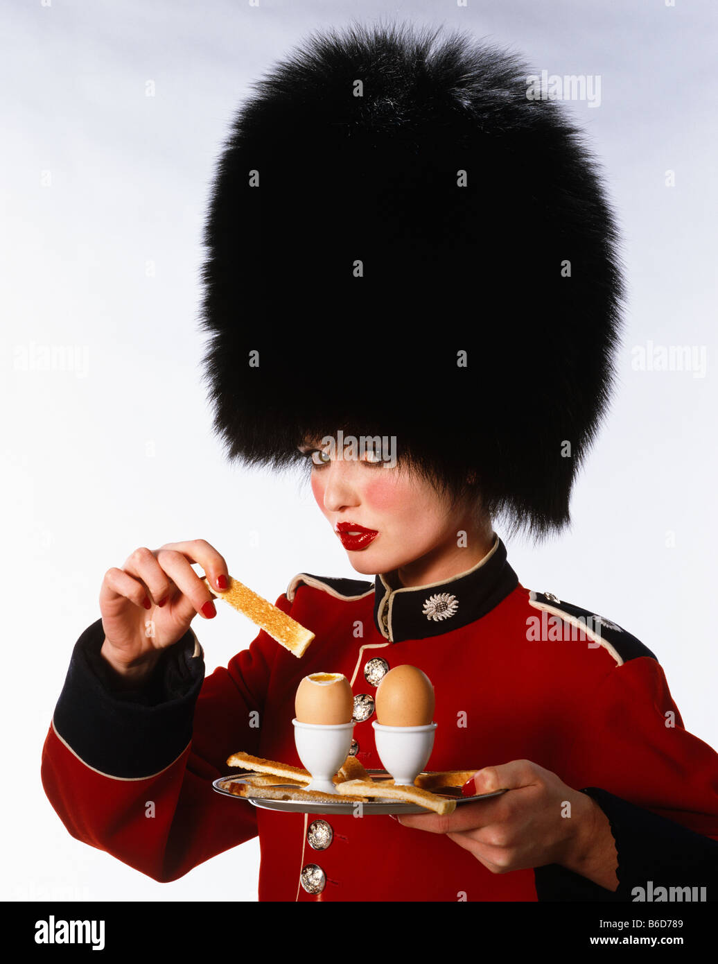Model dressed as a solidier (Grenadier Guard) dipping bread soldiers into boiled egg yolk Stock Photo