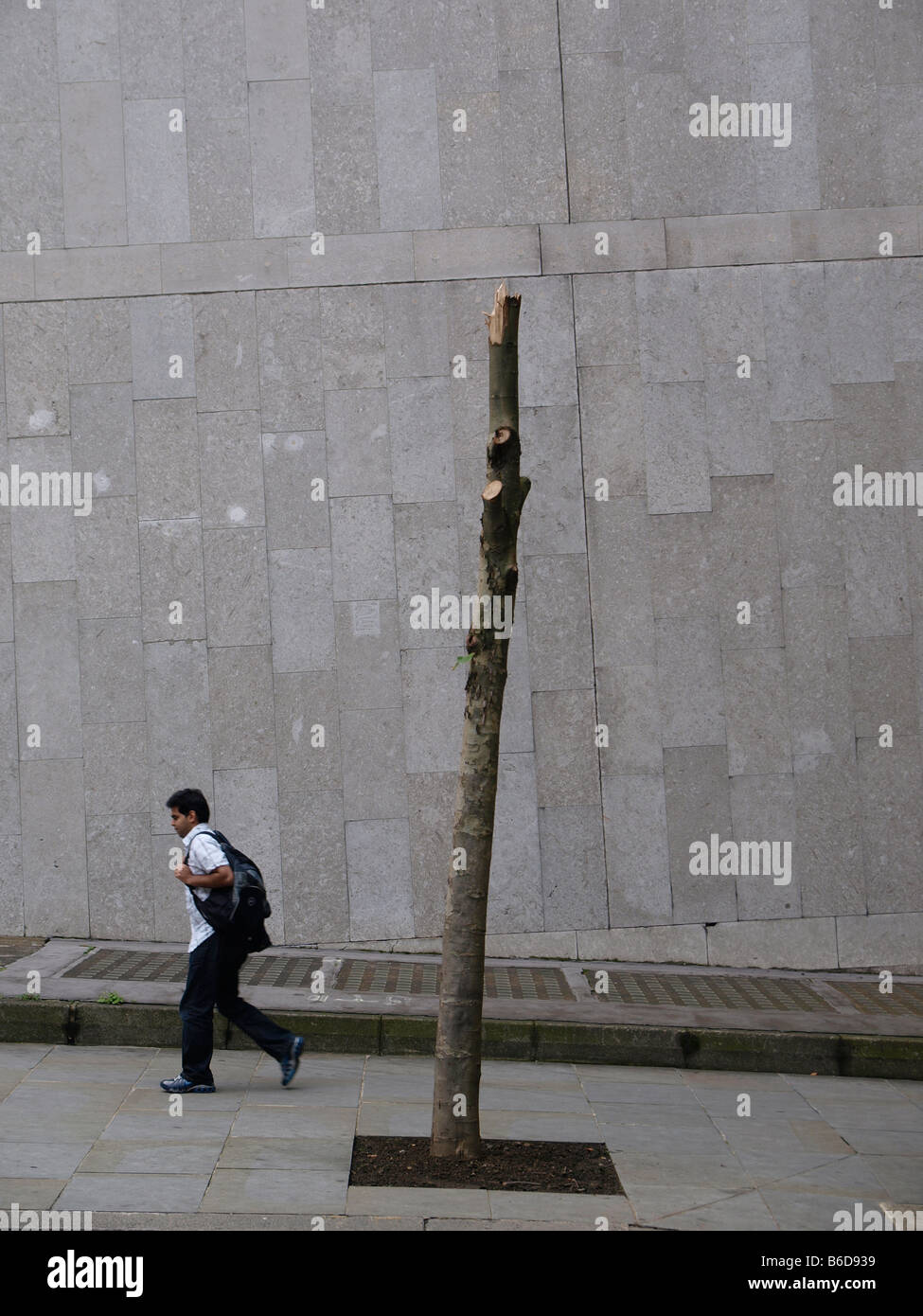 Strange urban scene with man walking up slope and weird looking tree remains London UK Stock Photo
