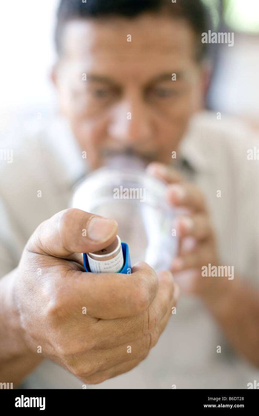 Asthma spacer use. Man using an asthma spacer with a blue asthma
