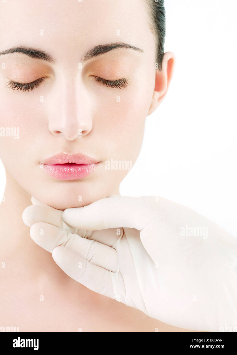 Cosmetic surgery. Conceptual image of cosmetic surgery represented by a gloved hand touching a woman's face. Stock Photo