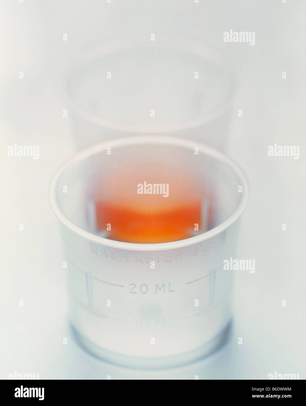 Cup of medicine. Two plastic cups, one containing a liquid medicine. The cups are marked to measure the dose. Stock Photo
