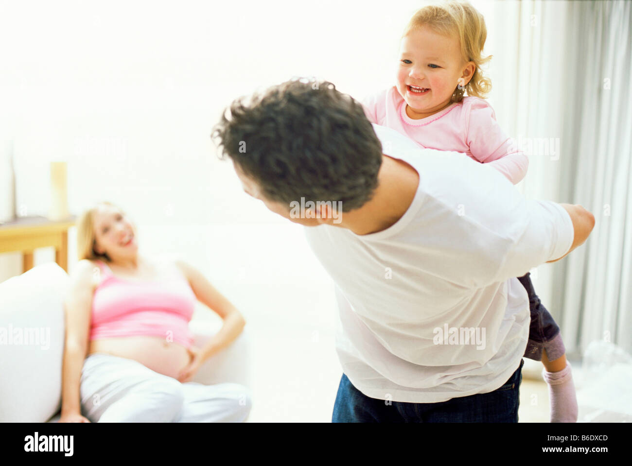 Father giving piggyback ride to daughter while mother sitting in background Stock Photo