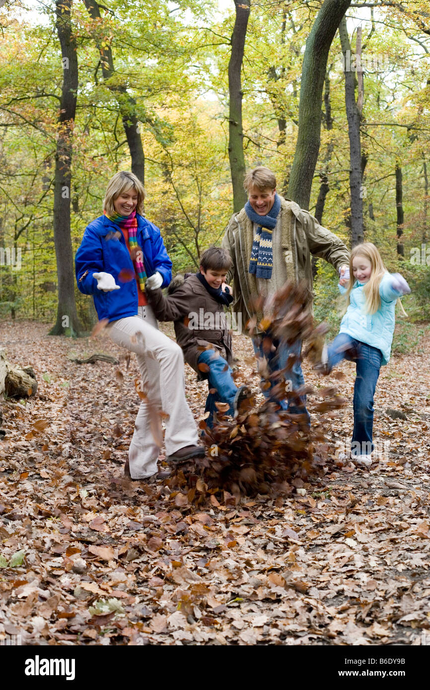 Kicking autumn leaves. Mother and father and son and daughter kicking leaves in a wood in autumn. Stock Photo