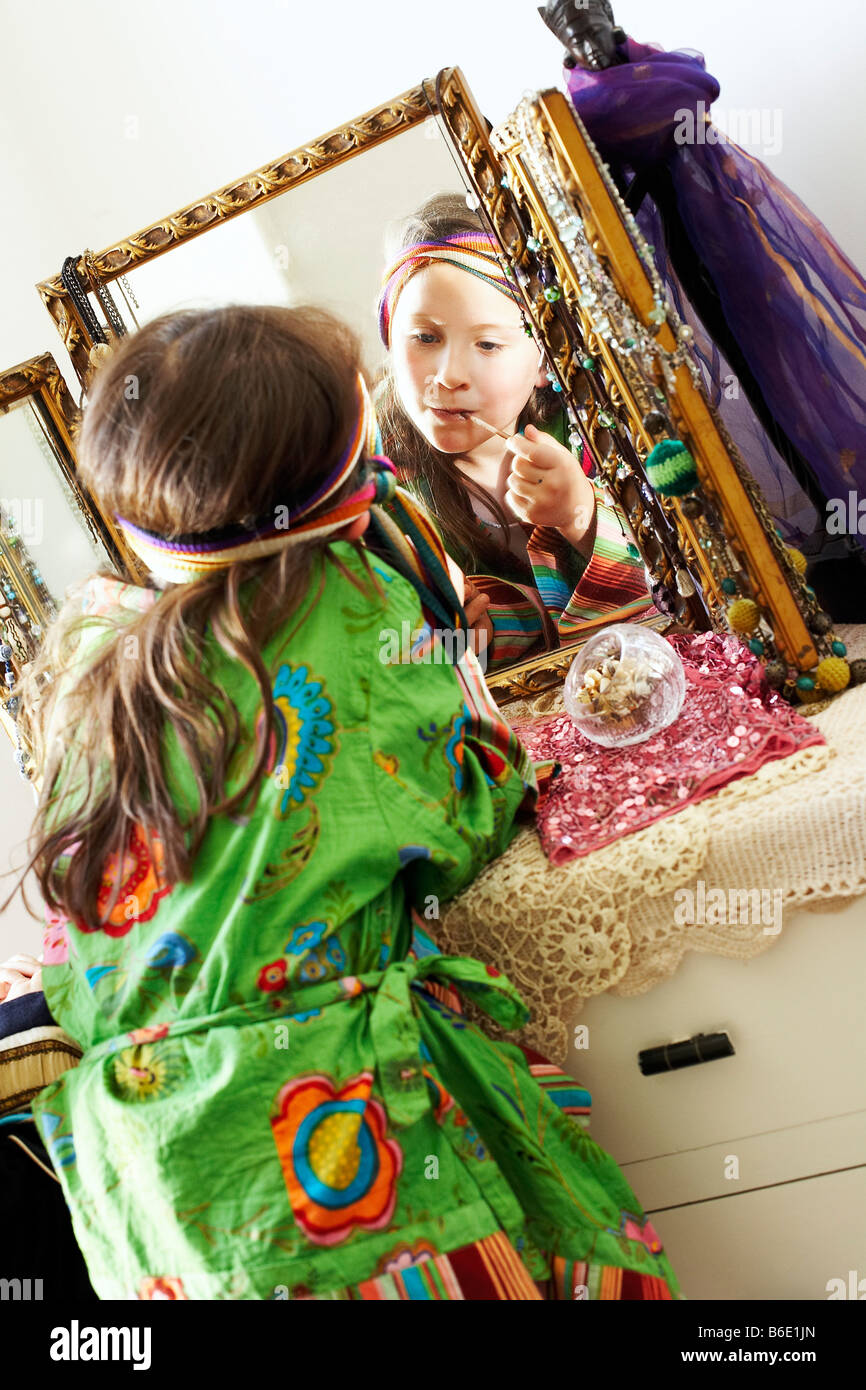 Dressing up. Young girl using a mirror to apply lipstick during a