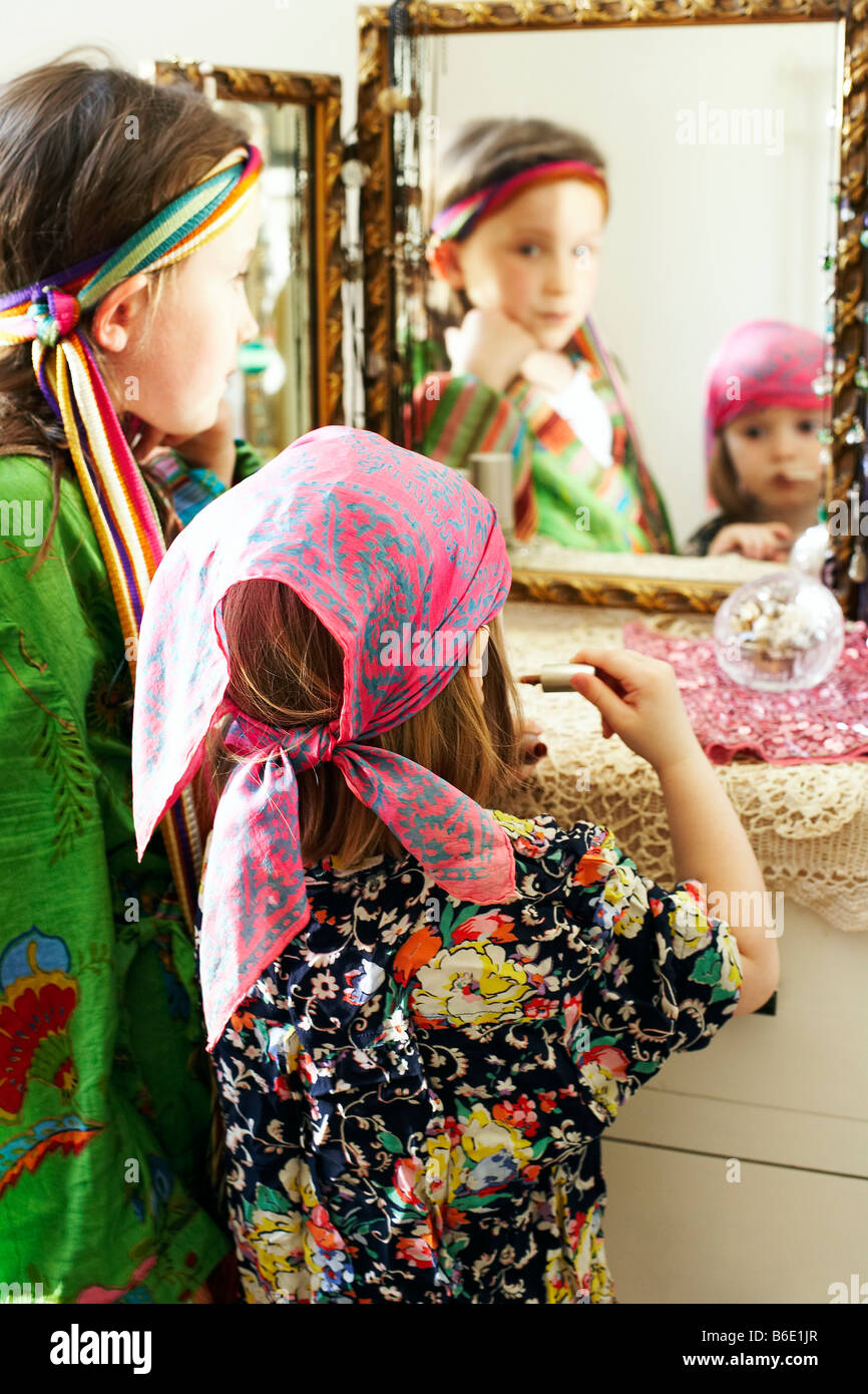 Dressing up. Four year old girl using a mirror to apply lipstick during