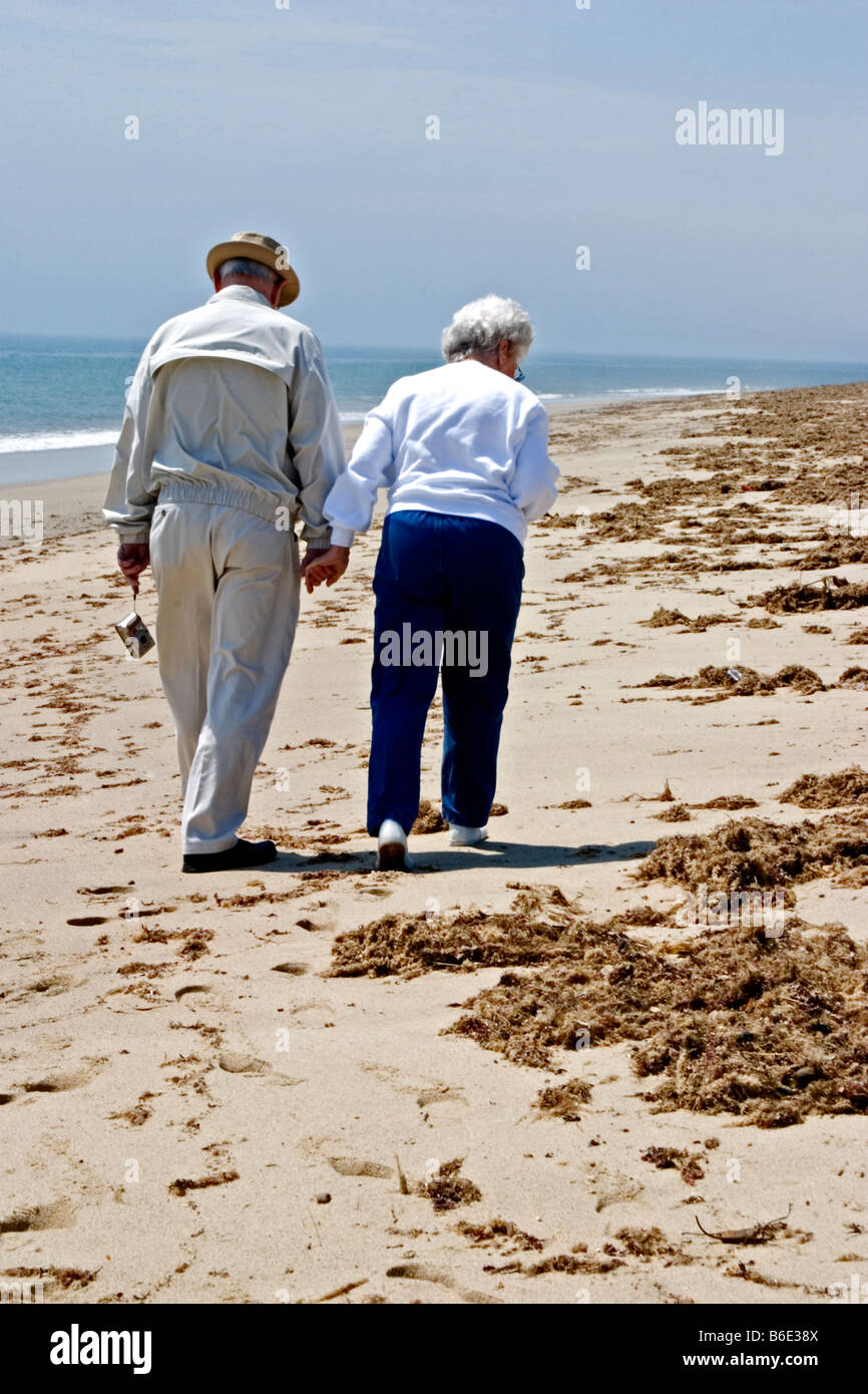 A senior citizen couple walking along the beach looking for shells Stock Photo