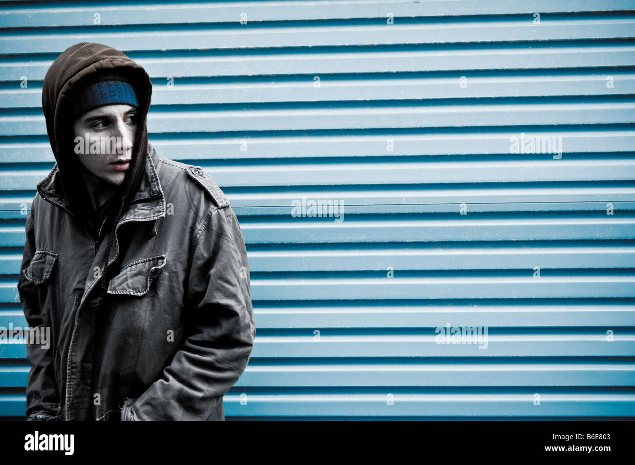 Young man wearing a hooded jacket alone and isolated looking vulnerable and under threat Stock Photo