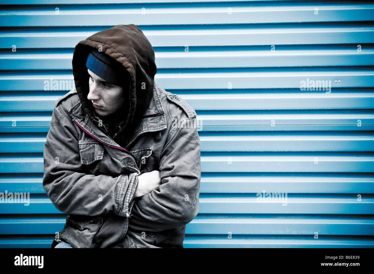 Young man wearing a hooded jacket alone and isolated looking vulnerable and under threat Stock Photo