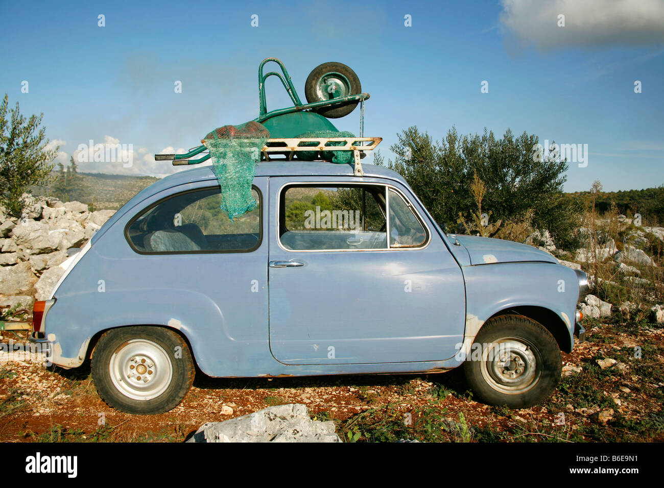 Little blue car with wheel barrow on roof Stock Photo