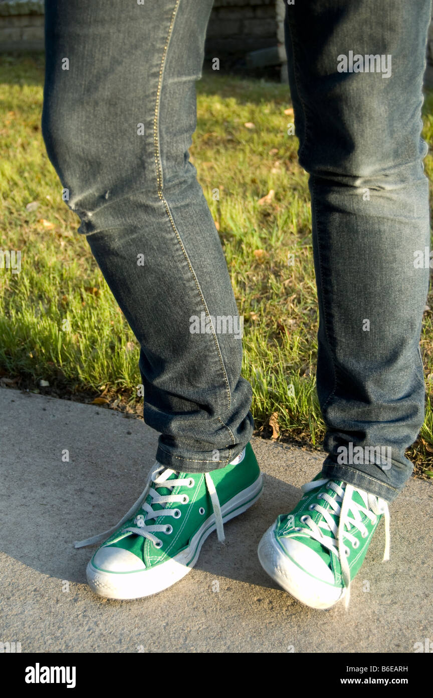 A teenage girls legs wearing skinny blue denim jeans and green Converse  sneakers on her feet Stock Photo - Alamy