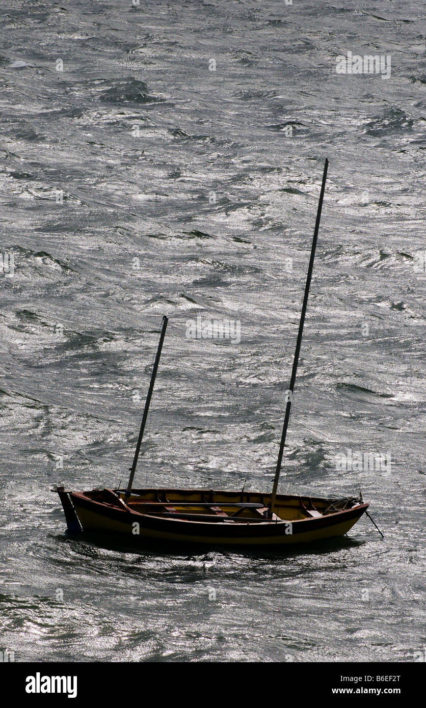 A yellow sail-boat, masts down rocks back and forth on the stormy seas in a strong wind. Solitude, peace, rest and relaxation. Stock Photo