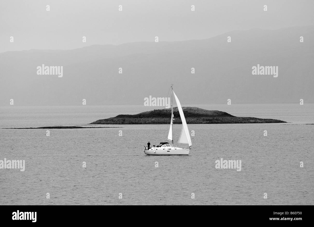 A luxurious yacht sailboat catches strong breeze as it sails across the open ocean with rocky islands in the background freedom Stock Photo