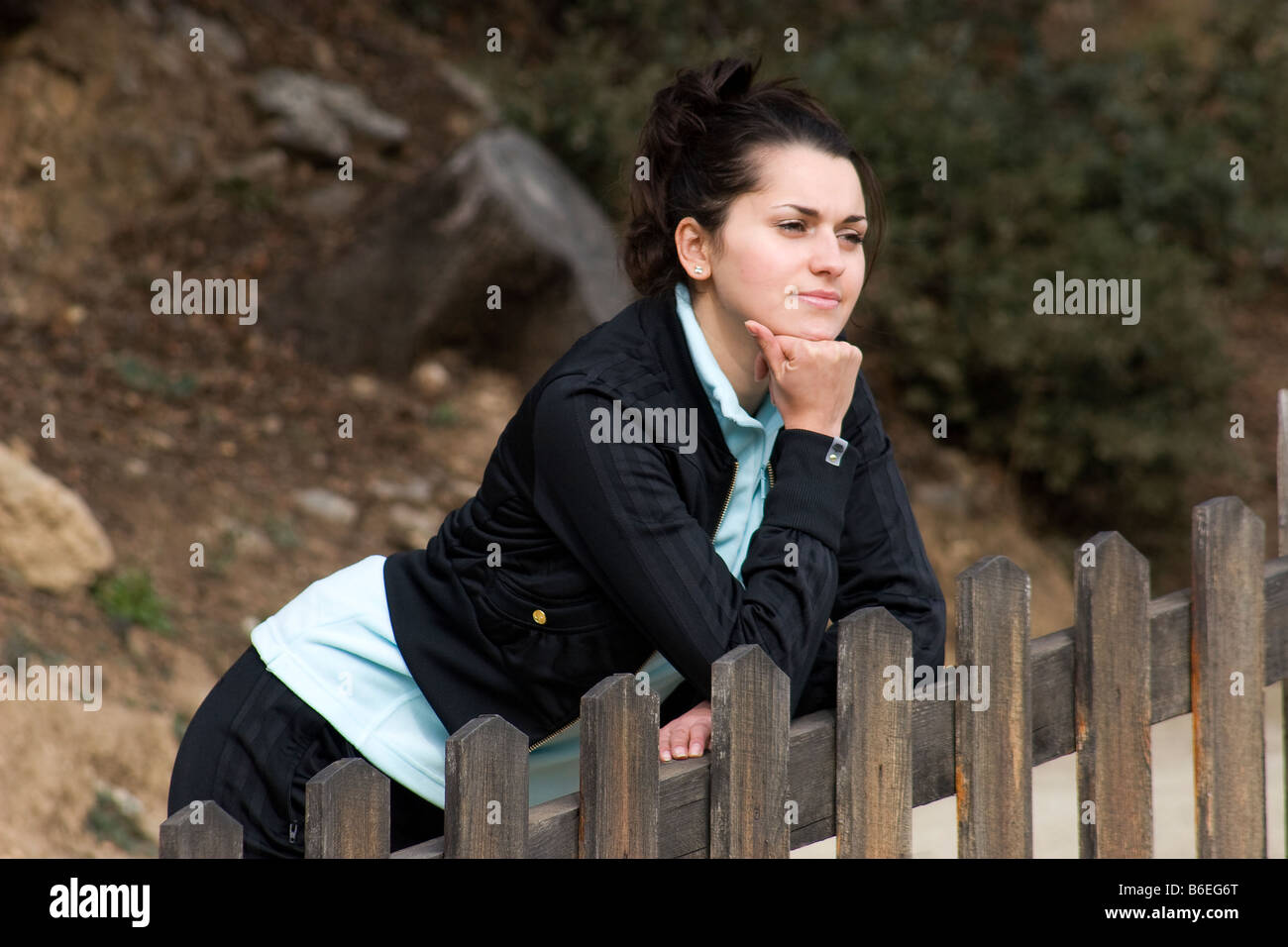 portrait sad looking young woman standing by fence Stock Photo