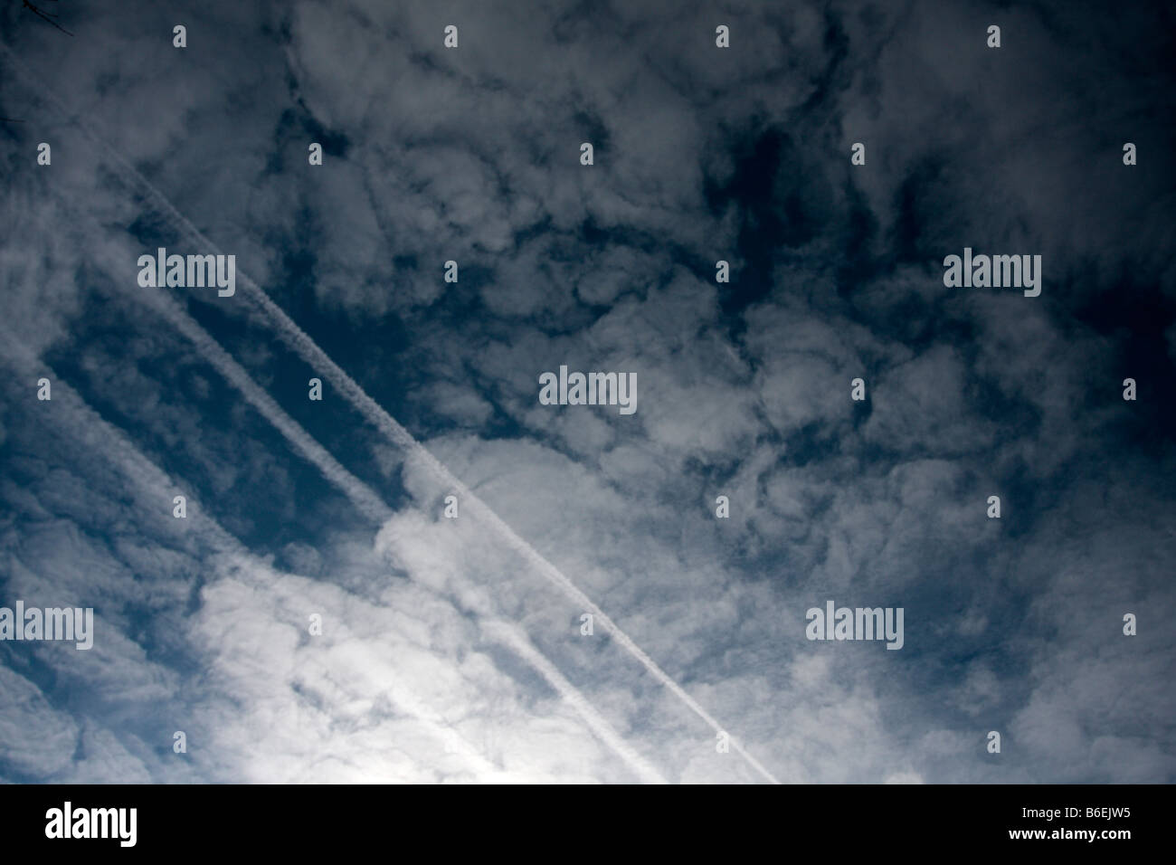 Cloudy sky diagonally crossed by 3 contrails. Stock Photo
