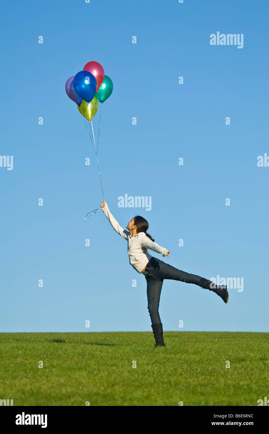 A young girl (11) 'lifted' in the air by a bunch of colourful helium filled balloons against a blue sky. Stock Photo