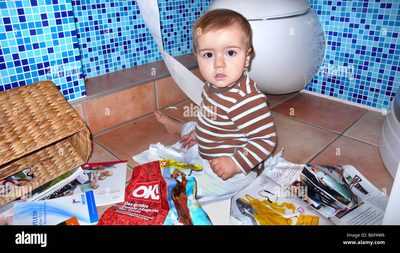 little boy sitting on the bathroom floor among tattered magazines Stock Photo