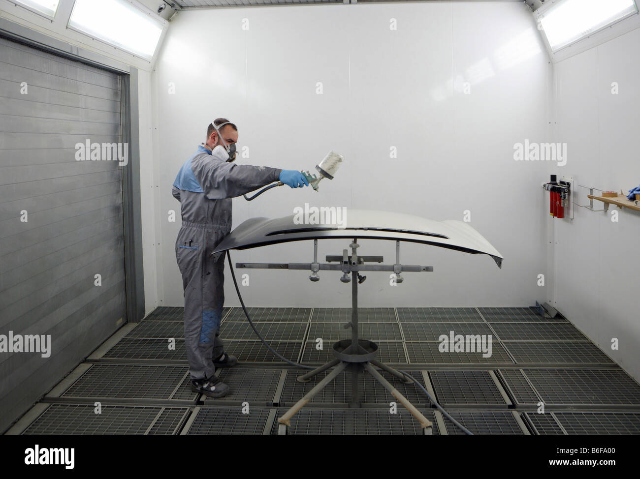 Painter spraypaints a vehicle body panel with a spray gun in a sealed spraying room at the Daimler AG, Mercedes Benz Plant in S Stock Photo