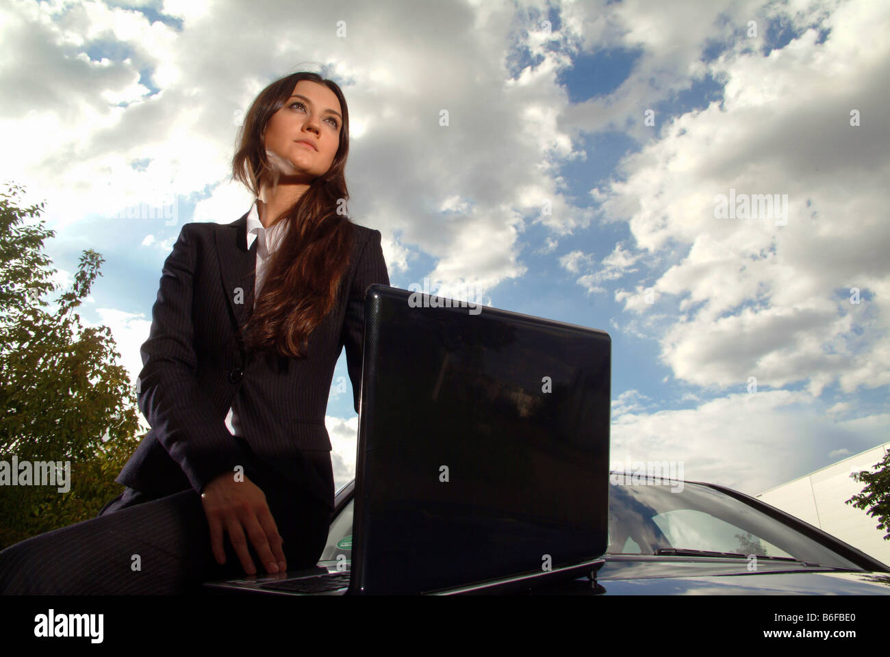 Young businesswoman in her car with a laptop in front of a cloudy sky Stock Photo
