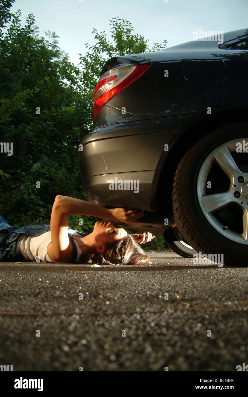 Young woman in working clothes is lying under her car while fixing it Stock Photo