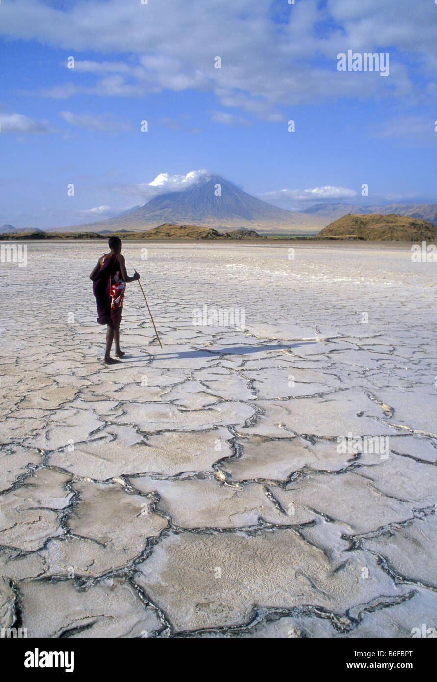 Maasai warrier walking on the dired-out soda-lake called Lake Natron in northern Tanzania, in the background is the holy mounta Stock Photo