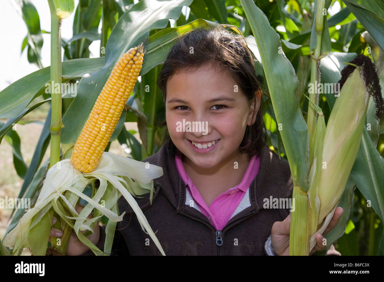 Smiling girl, about 11, next to a corn cob in a field of maize