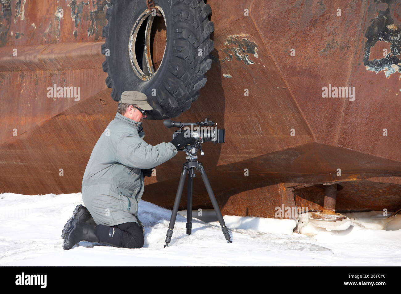 Photographer filming in front of rusted ship, Amguema, Chukotka,  Russia Stock Photo