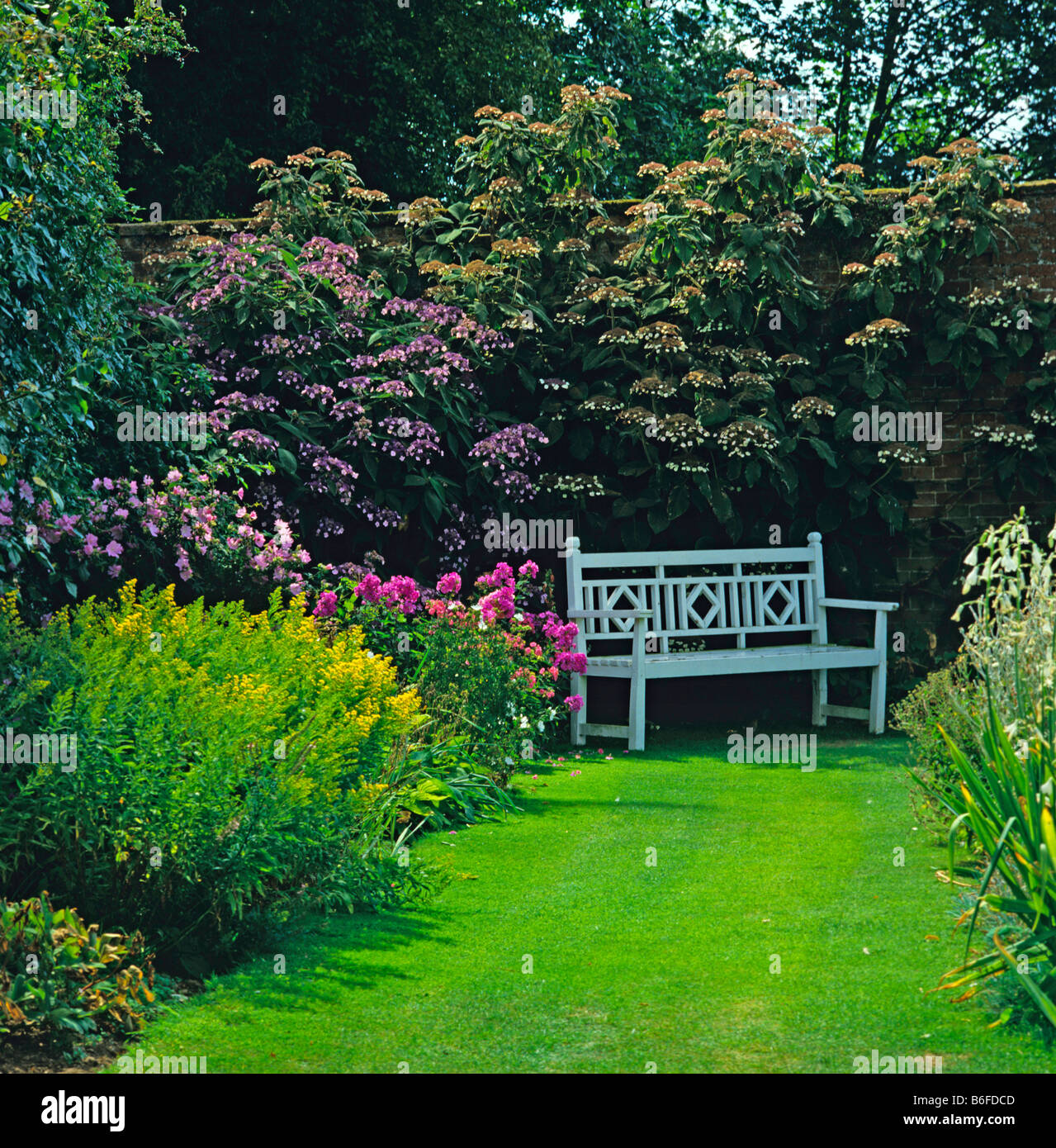 Romantic seat in walled garden with a colourful flower borders Stock Photo