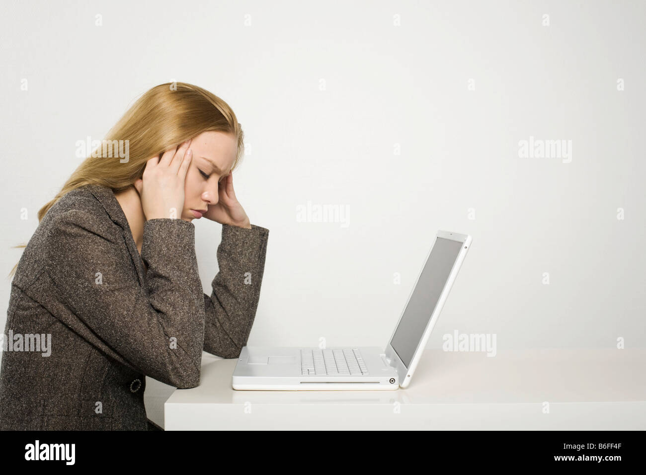 Young long-haired woman sitting bored and tired in front of a notebook Stock Photo
