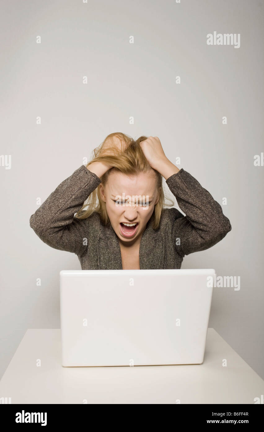 Young long-haired woman yelling in despair at her computer, notebook, tearing her hair Stock Photo