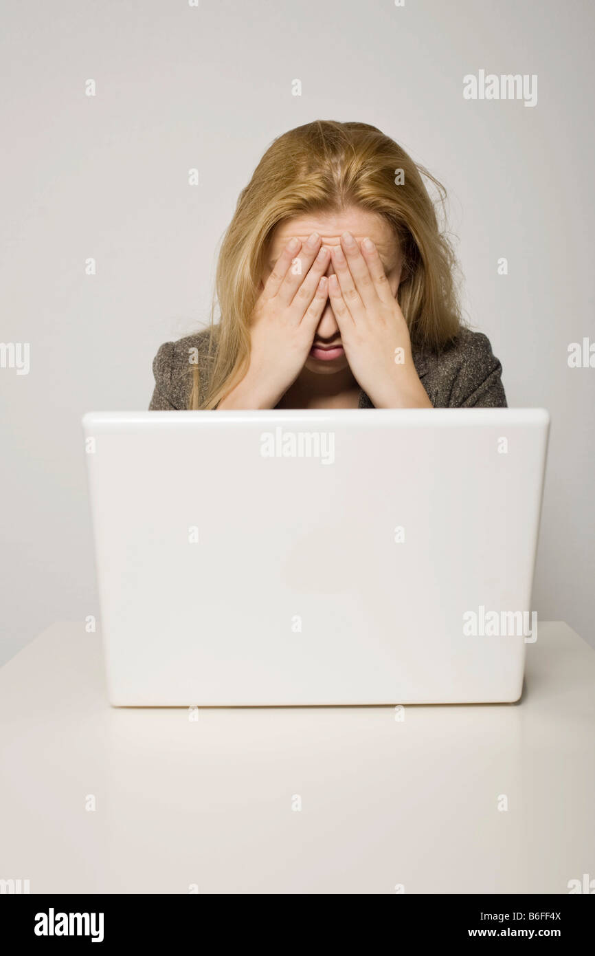 Young long-haired woman sitting frustatedly in front of her computer, notebook, her hands covering her face Stock Photo