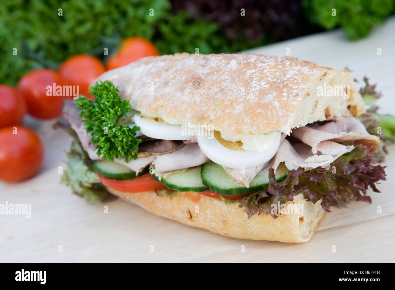 Onion baguette with salad, tomatoes, cucumber, roast pork, egg and mayonnaise, decoration of lollo rosso and bianco, cherry tom Stock Photo