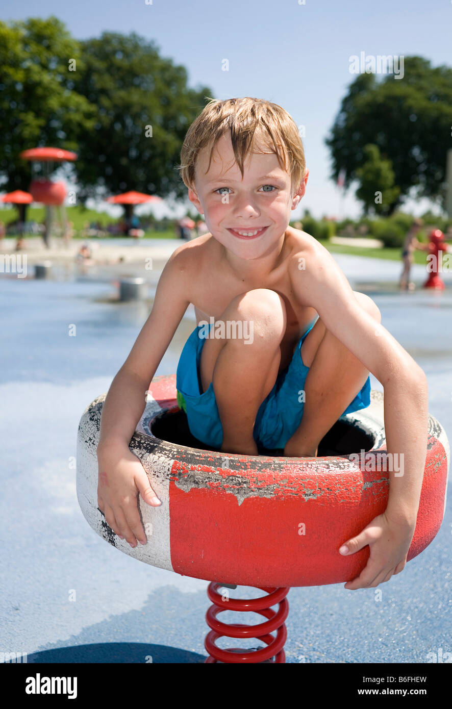 Boy, 6 year-old, sitting on a piece of playground equipment in a water park Stock Photo