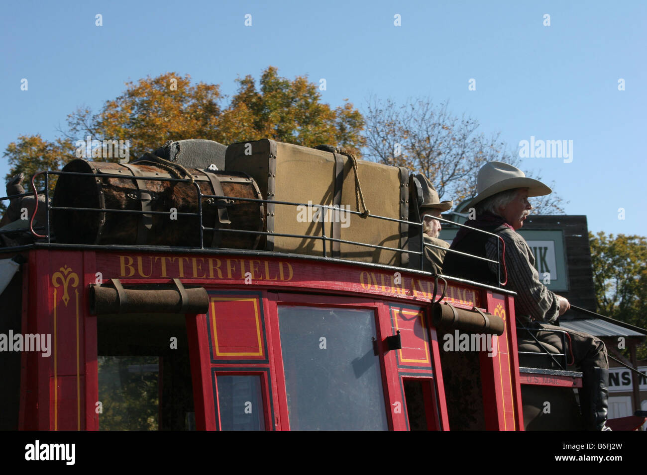 Two cowboys driving the Butterfield Overland Stage Coach through an old western town Stock Photo