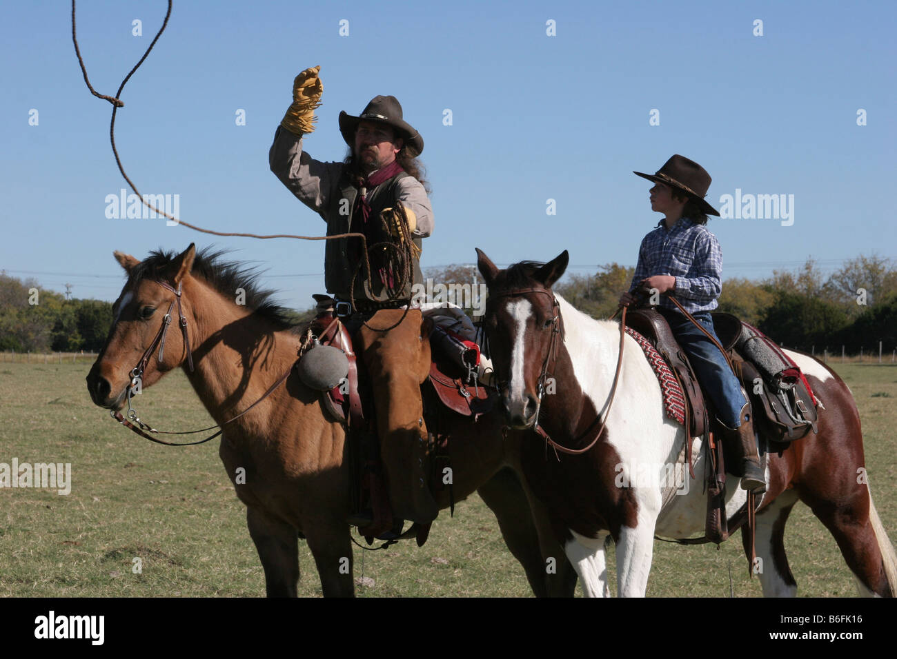 A cowboy father showing his son how to rope a cow on the ranch by throwing the rope Stock Photo