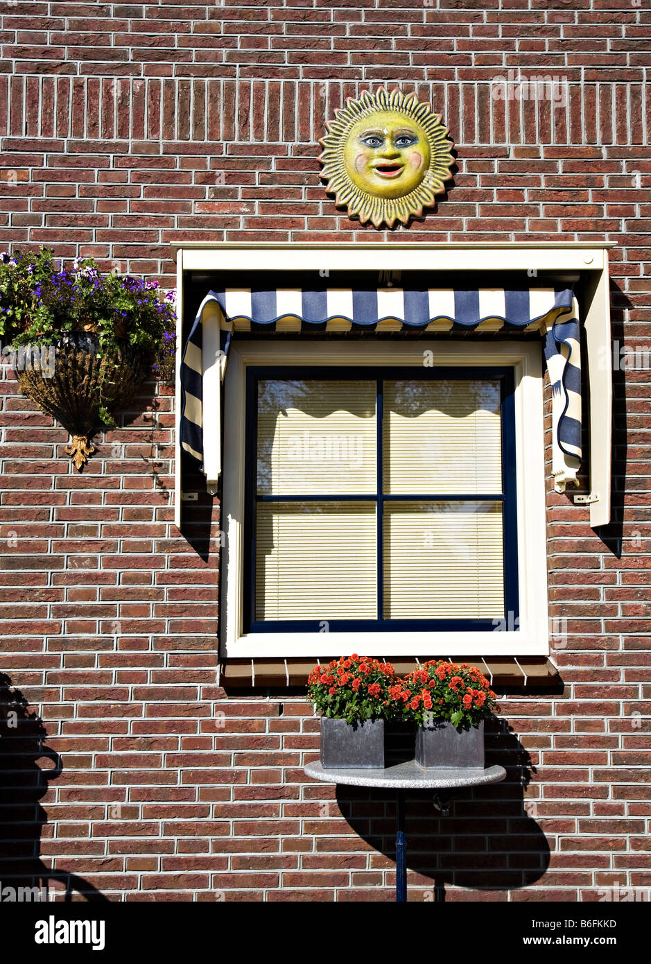 Window with blinds and flowers with ornamental sun face on brick wall