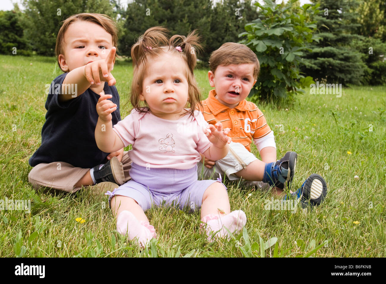 Three babies, 1 year, 8 months and 10 months, sitting on grass Stock Photo