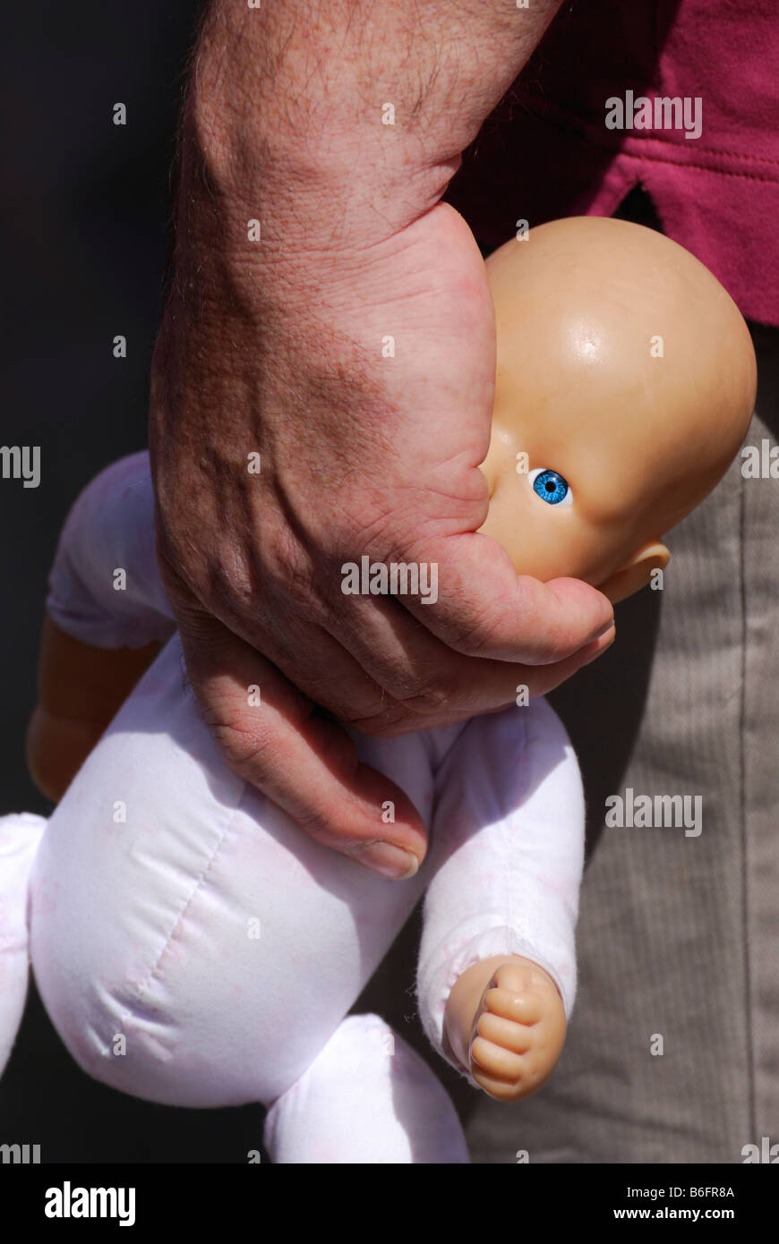 Meaty male hand carrying a doll by the neck, picture symbolizing violence against children, Emmendingen, Baden-Wuerttemberg, Ge Stock Photo