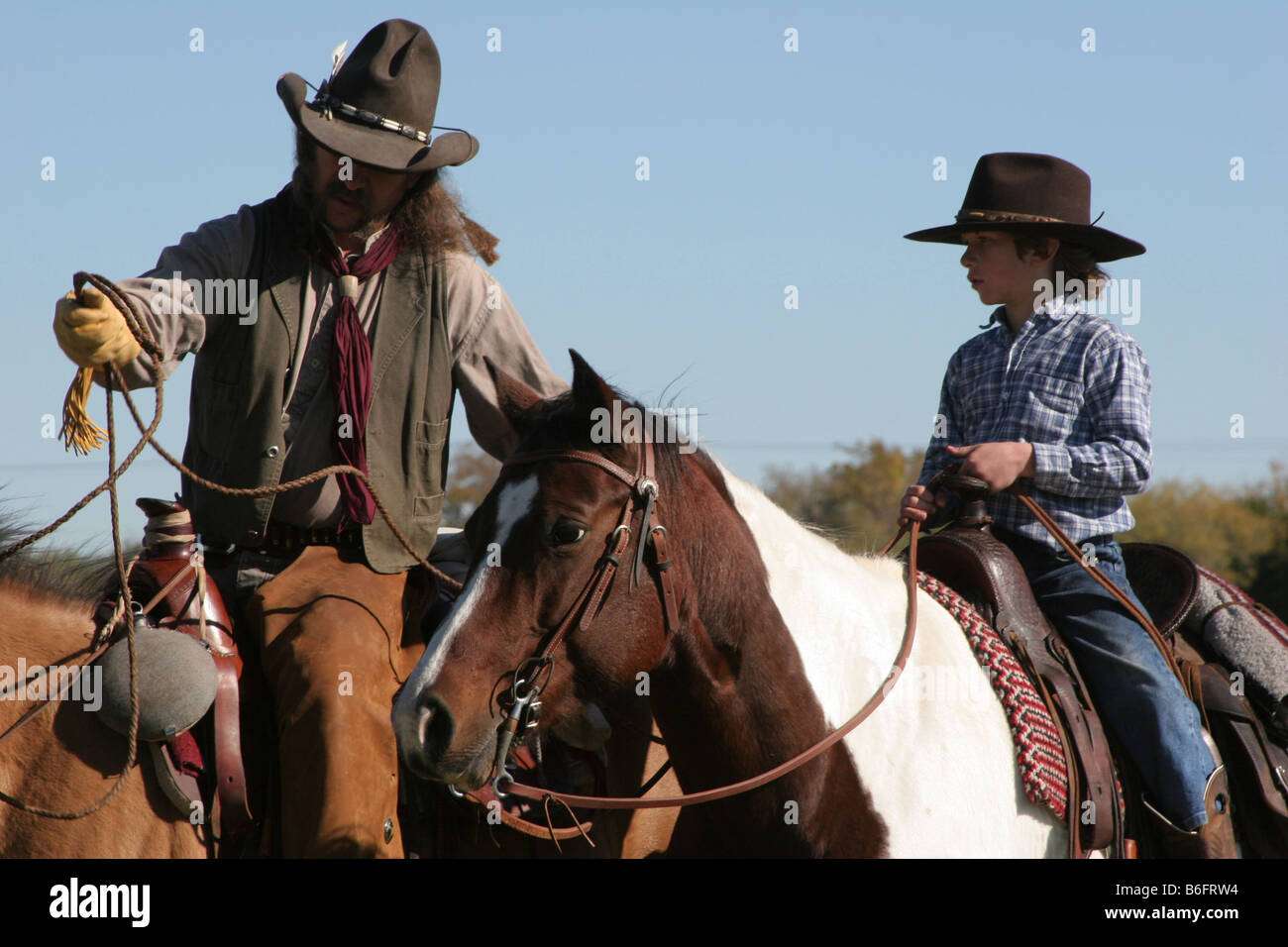 A cowboy father showing his son how to rope a cow on the ranch Stock Photo