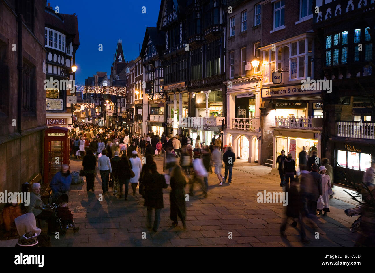 UK Cheshire Chester Eastgate Street Christmas lighting above shoppers at dusk Stock Photo