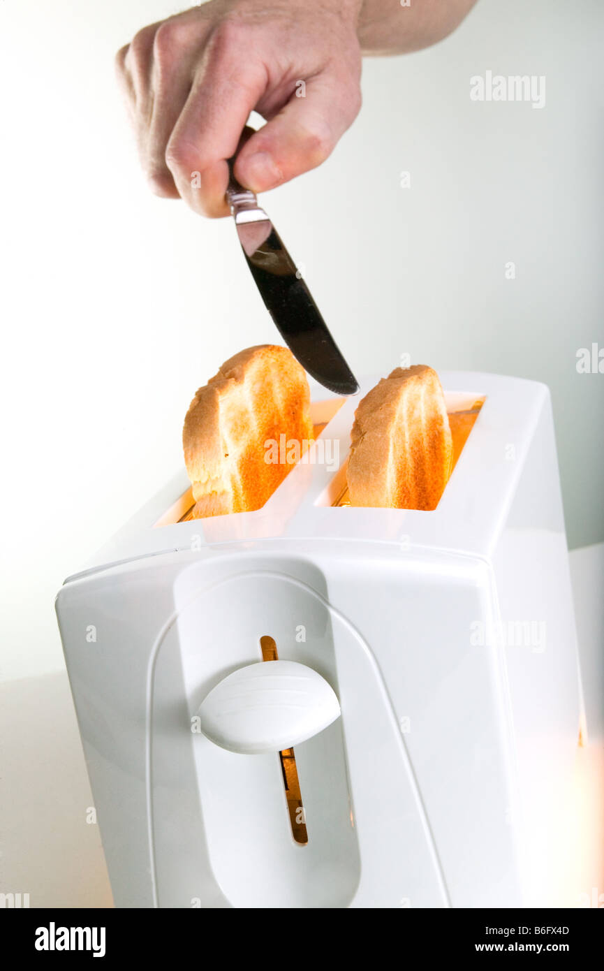 Hand sticking knife in white toaster Stock Photo - Alamy