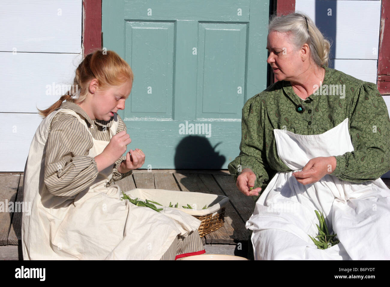 A grandmother and a young girl snapping beans on their farmhouse porch