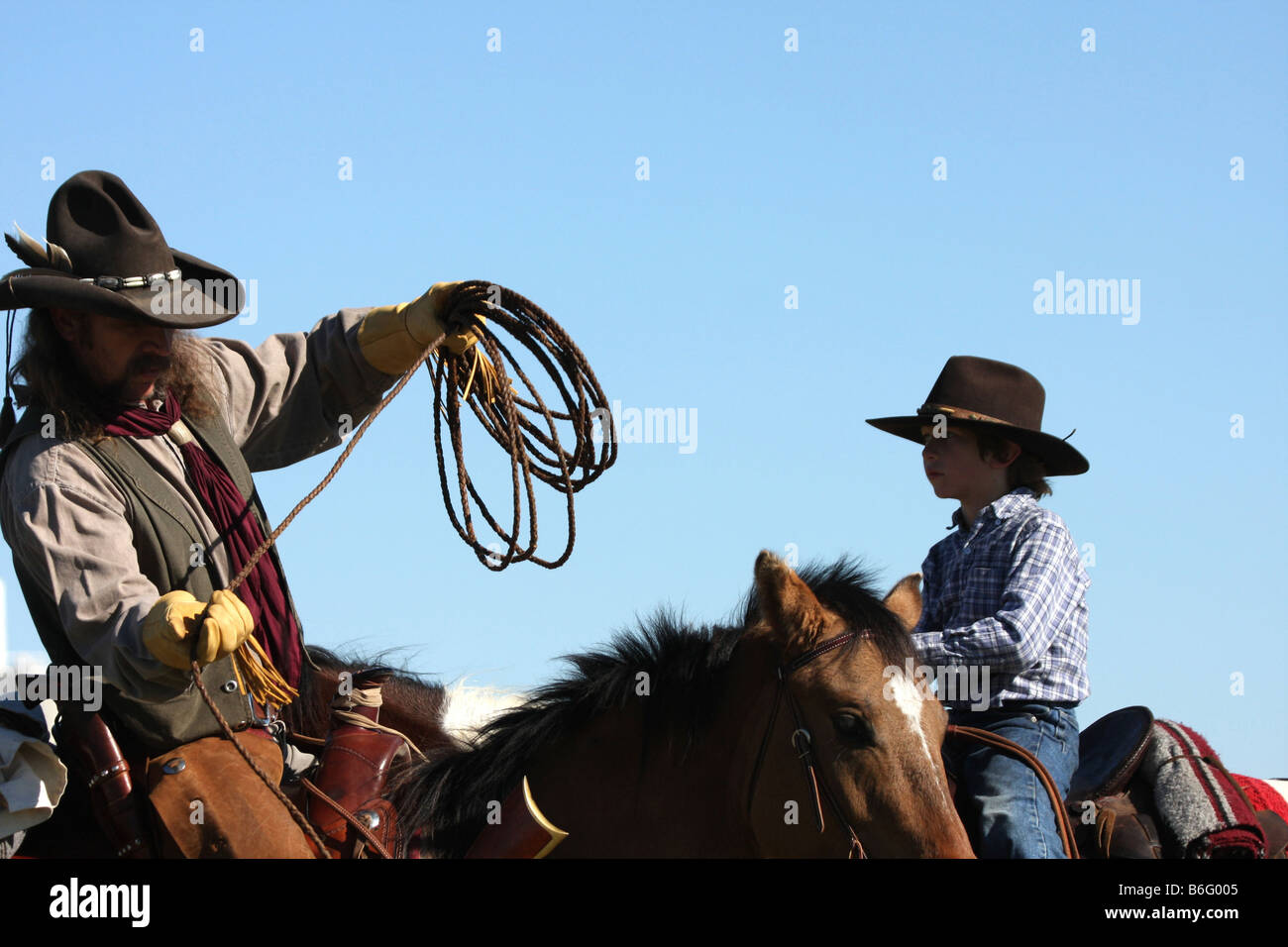 A cowboy father on horseback showing his son how to throw a rope to ...