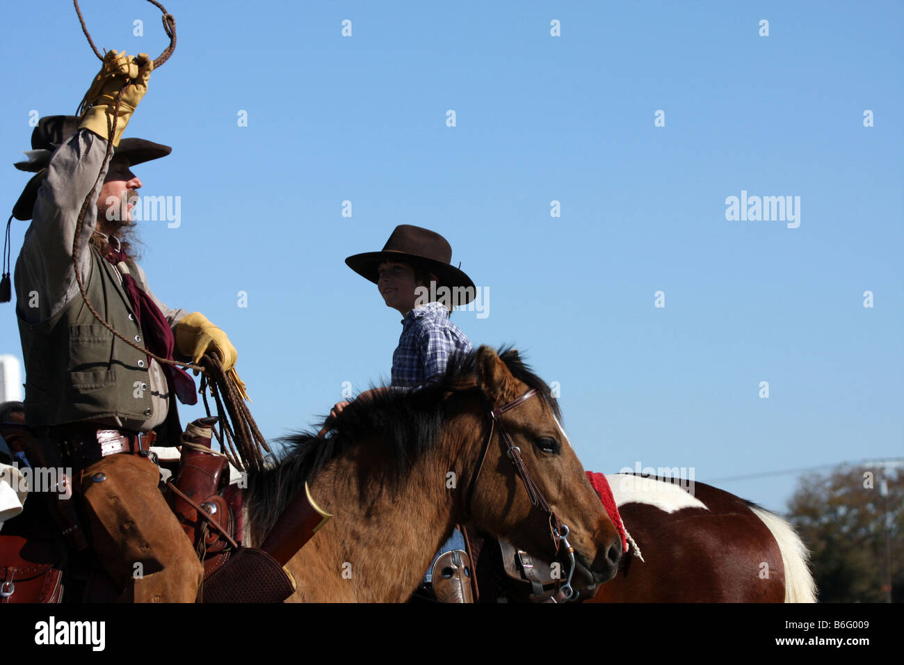 A cowboy father on horseback showing his son how to throw a rope to