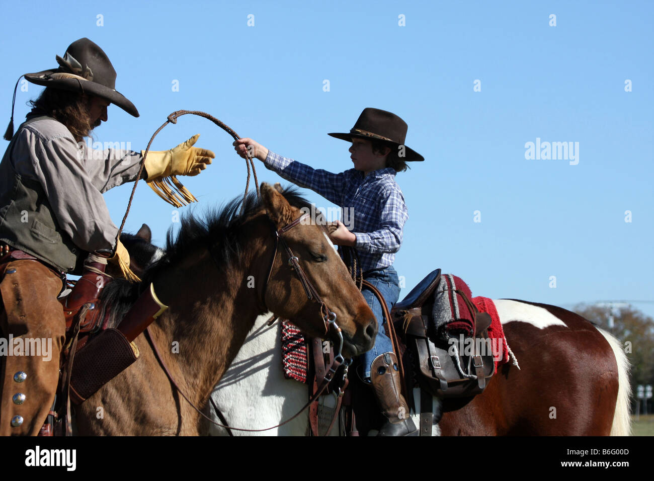 A cowboy father on horseback showing his son how to throw a rope to